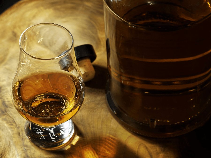 Glass of rum next to an opened bottle