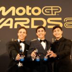 Three men hold beers in front of MotoGP sign