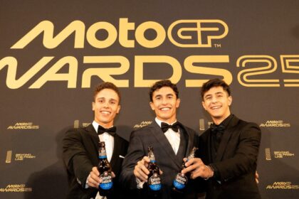 Three men hold beers in front of MotoGP sign