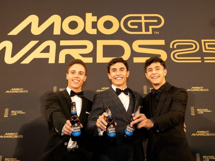 Three men hold beers in front of MotoGP sign