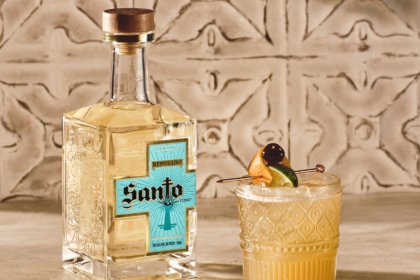 Bottle of Santo Tequila next to a cocktail against stone wall