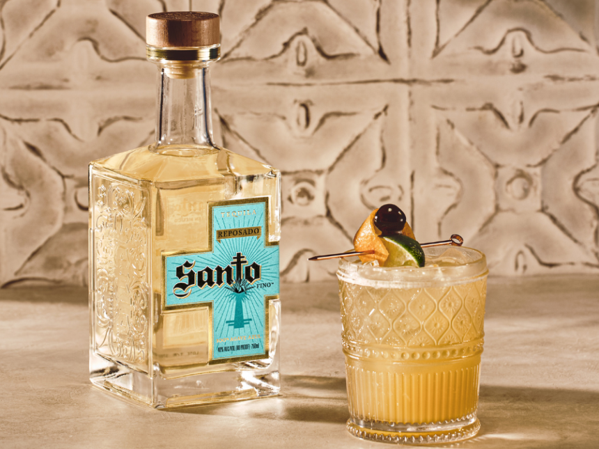 Bottle of Santo Tequila next to a cocktail against stone wall