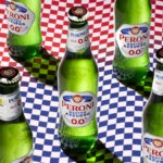 Bottles of Peroni Nastro Azzurro 0.0% against a chequered flag backdrop