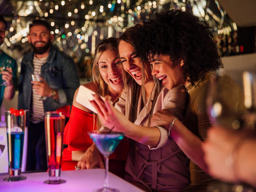 Three women at a bar with cocktails taking a selfie