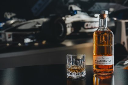Bottle of Coachbuilt blended scotch whisky in front of a Williams Racing F1 car