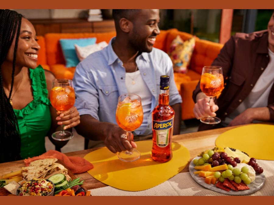 Three consumers with Aperol spritz serves and a bottle of Aperol