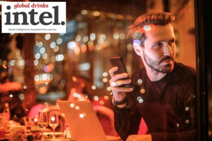 A man at a table in a bar looking at a cellphone with a laptop open