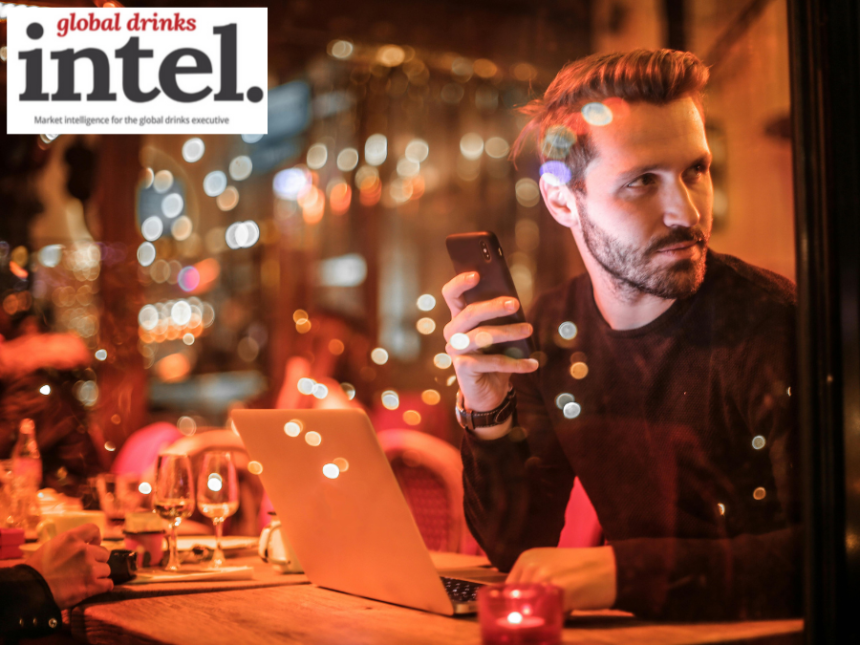 A man at a table in a bar looking at a cellphone with a laptop open