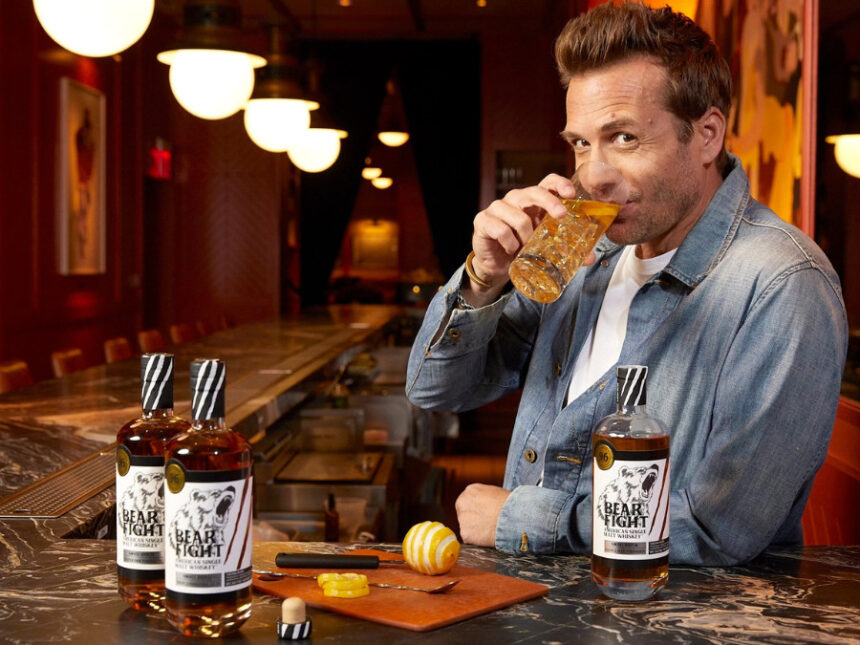 Two bottles of Bear Fight American whiskey on a bar with Gabriel Macht