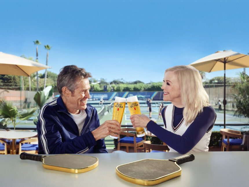 Willem Dafoe and Catherine O'Hara clinking Michelob Ultra beers