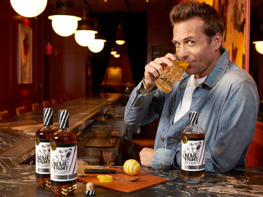Two bottles of Bear Fight American whiskey on a bar with Gabriel Macht