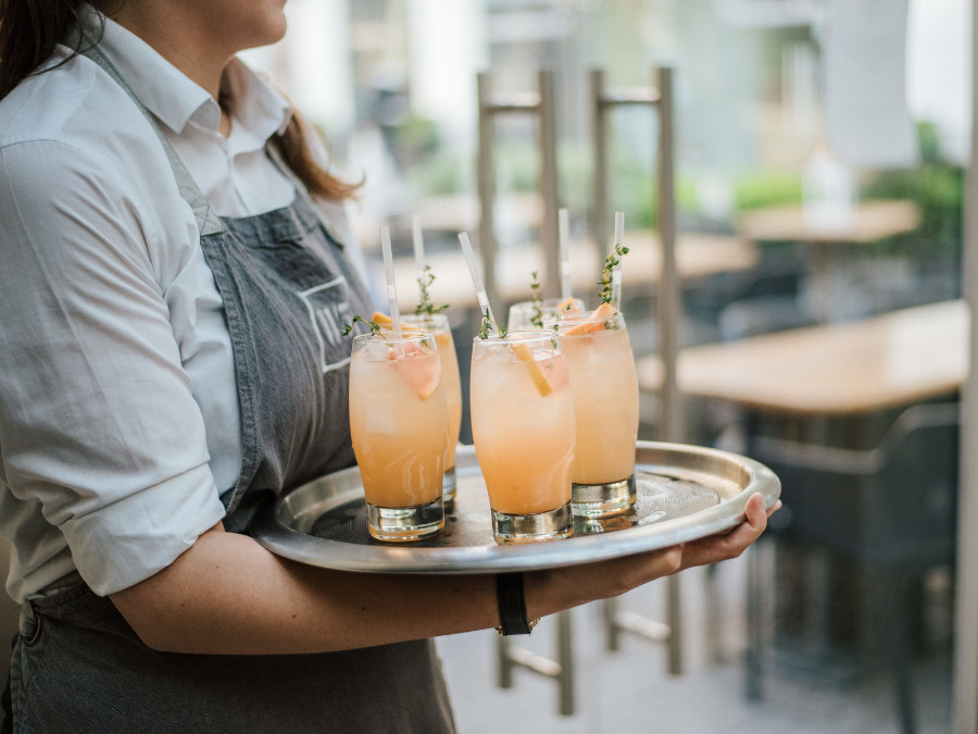 Table staff carrying a tray of four long drinks