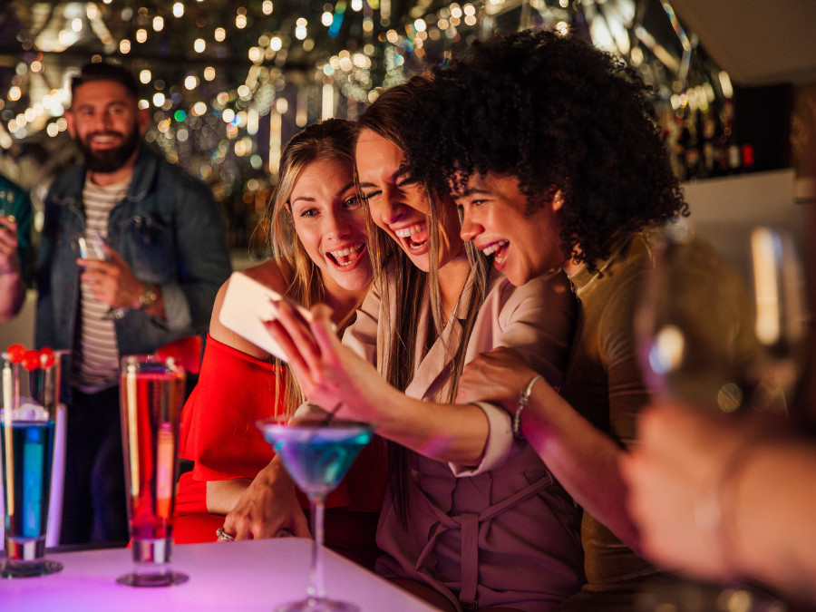 Three female consumers at a bar with drinks posing for a selfie