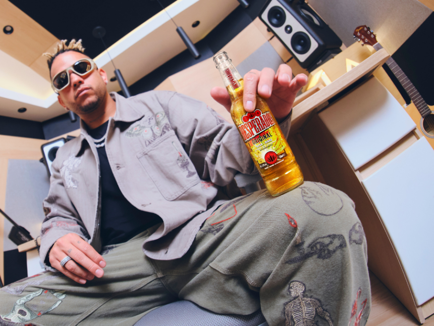 Ovy on the Drums holding a bottle of Desperados