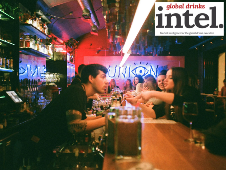 A bartender speaking to drinkers in a crowded bar