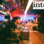 A bartender speaking to drinkers in a crowded bar