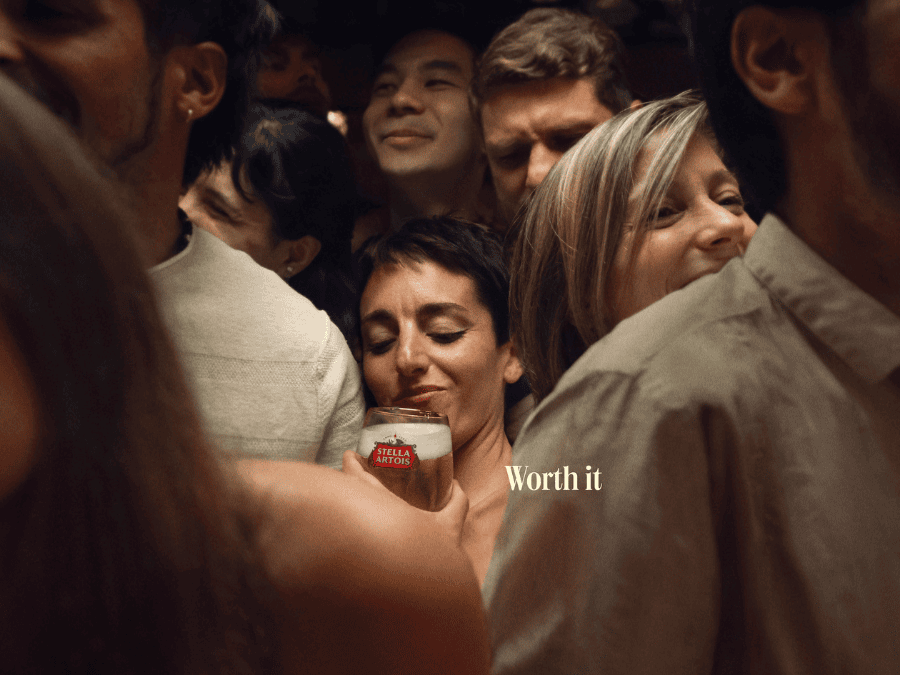 Person holding Stella Artois in crowded bar with 'Worth It' tagline