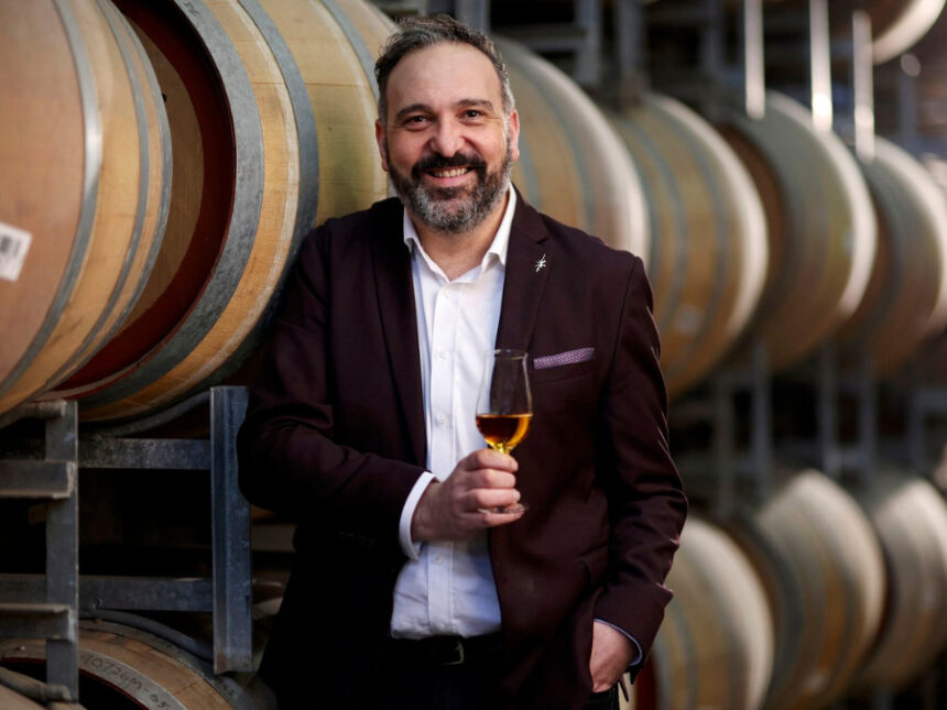 White man smiles holding whisky glass in a barrel room