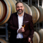 White man smiles holding whisky glass in a barrel room