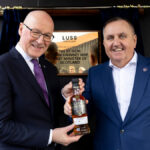 First Minister John Swinney Opens Luss-Distillery in Scotland, pictured with CEO Colin Matthews holding a bottle of whiskey in front of a plaque