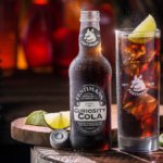 Bottle of cola on a table next to a glass with lime