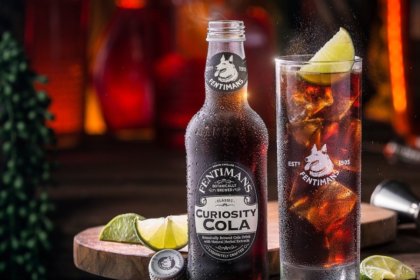 Bottle of cola on a table next to a glass with lime