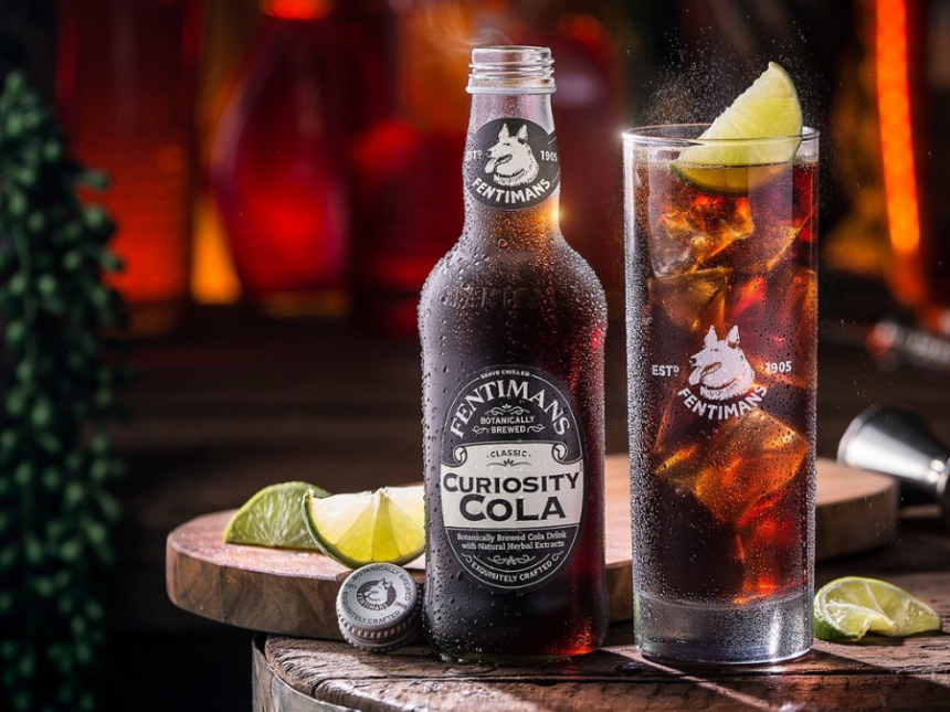 Bottle of cola on a table next to a glass with lime