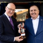 First Minister John Swinney Opens Luss-Distillery in Scotland, pictured with CEO Colin Matthews holding a bottle of whiskey in front of a plaque