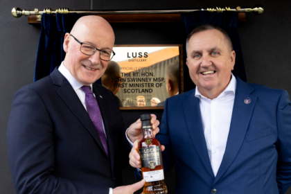 First Minister John Swinney Opens Luss-Distillery in Scotland, pictured with CEO Colin Matthews holding a bottle of whiskey in front of a plaque