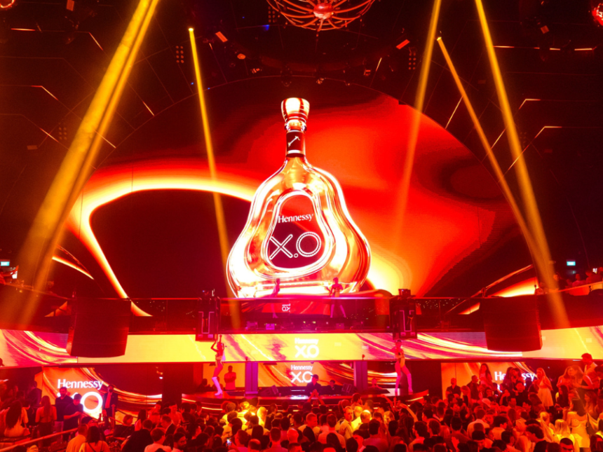 A giant bottle of Hennessey on a stage with red strobe lighting