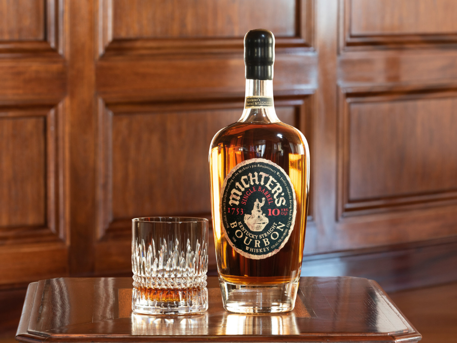 Bottle of Michter's Bourbon next to a glass on a wood table with wood panelling behind