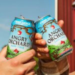Two hands cheers two cans of angry orchard cider