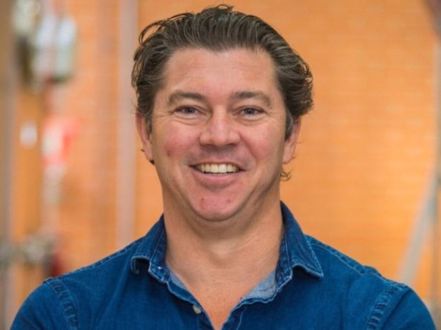 Headshot of white smiling man in denim shirt in a brewery