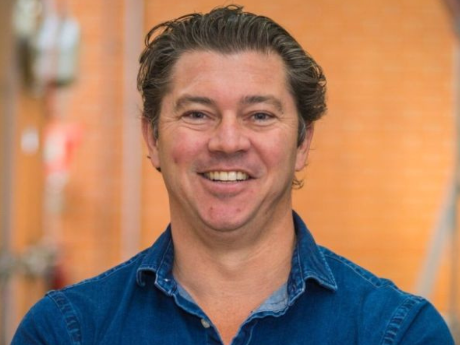 Headshot of white smiling man in denim shirt in a brewery