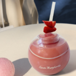 A forze cocktail in a ball shaped glass next to pink tennis balls