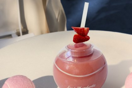 A forze cocktail in a ball shaped glass next to pink tennis balls