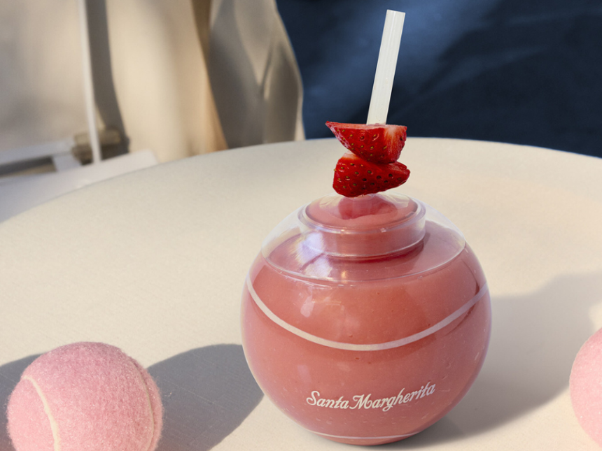 A forze cocktail in a ball shaped glass next to pink tennis balls