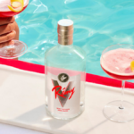 White spirit Remy V on a sun bed with stripey towel and two hands holding red cocktails either side