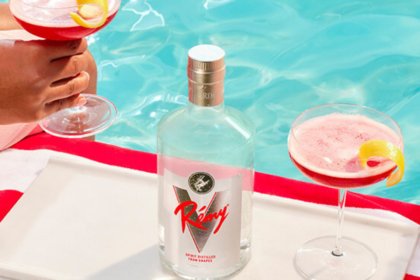White spirit Remy V on a sun bed with stripey towel and two hands holding red cocktails either side